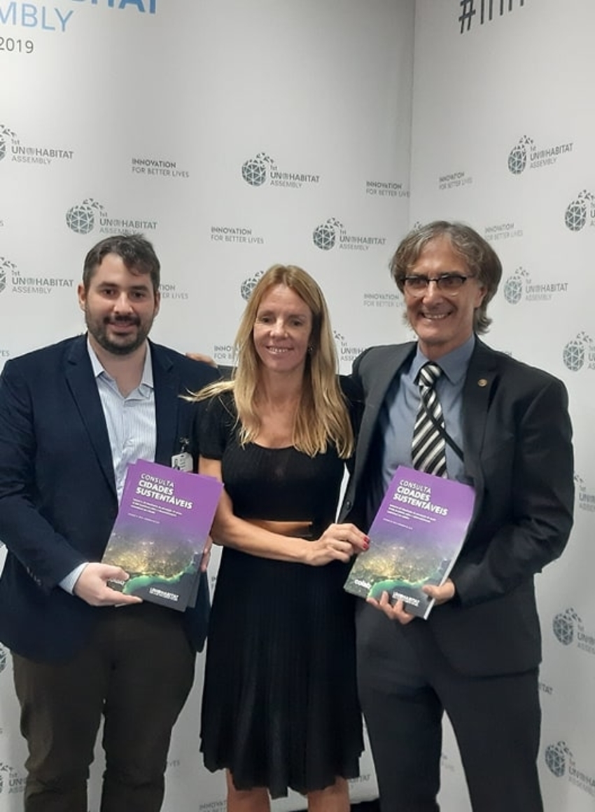 Three people stand in front of a wall holding a newly released publication.